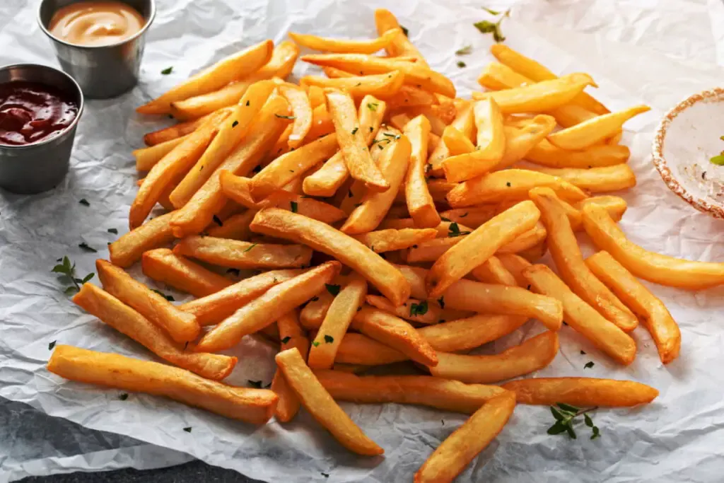 fried french fries on a parchment paper with ketchup and mustard dip