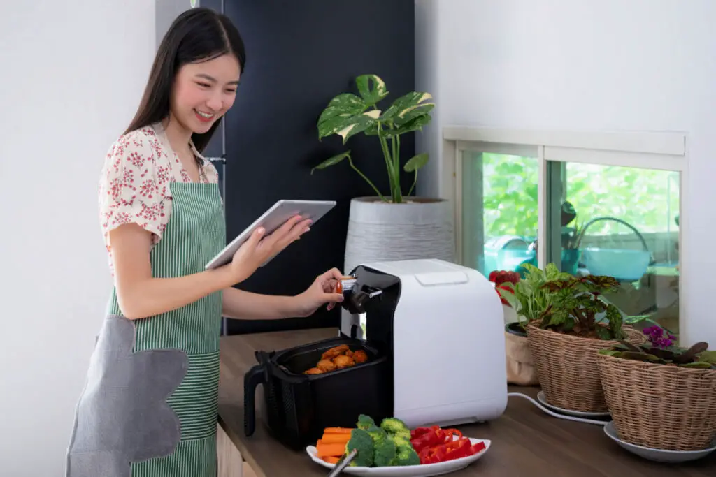 young girl reading on a tablet while cooking using an air fryer