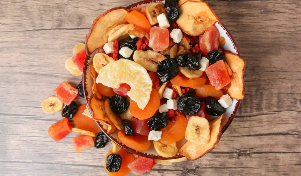 Bowl and different tasty dried fruits on wooden table, flat lay