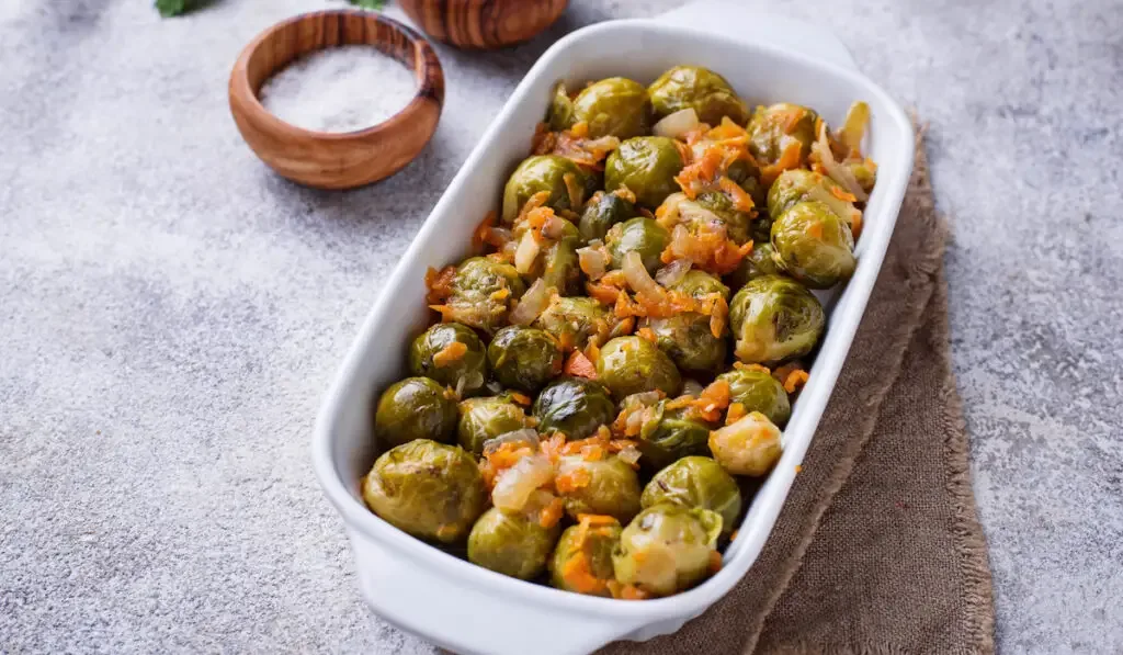 Baked brussels sprouts with carrot on white tray on gray table