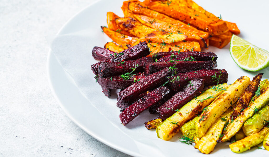 Roasted slices of zucchini, sweet potato and beetroots on white play on white background