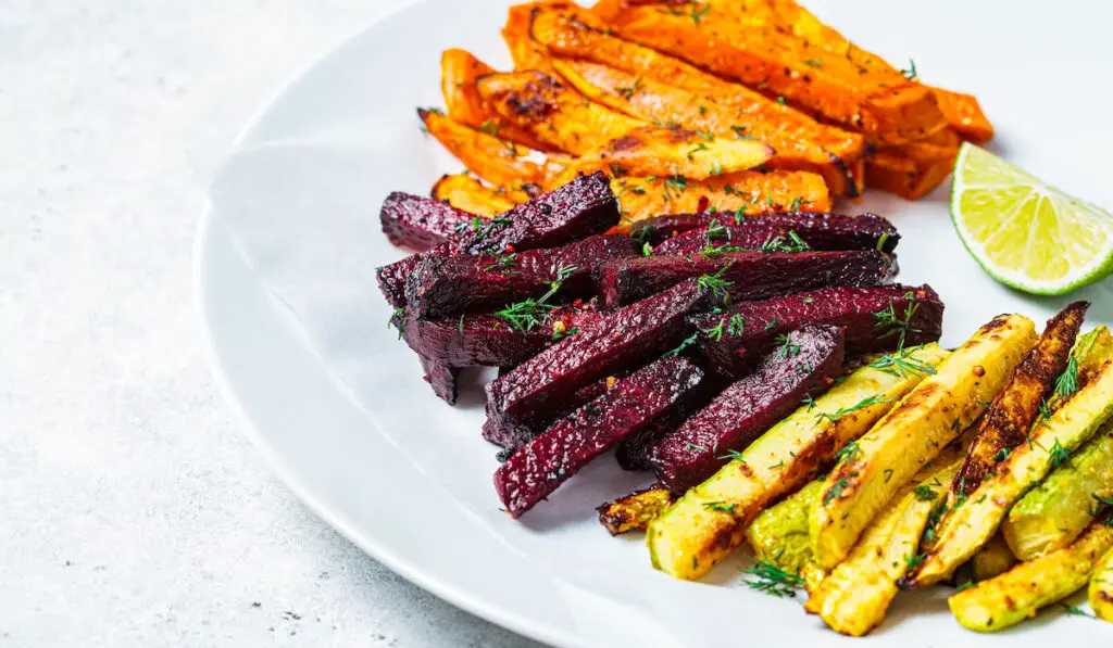 Roasted slices of zucchini, sweet potato and beetroots on white play on white background