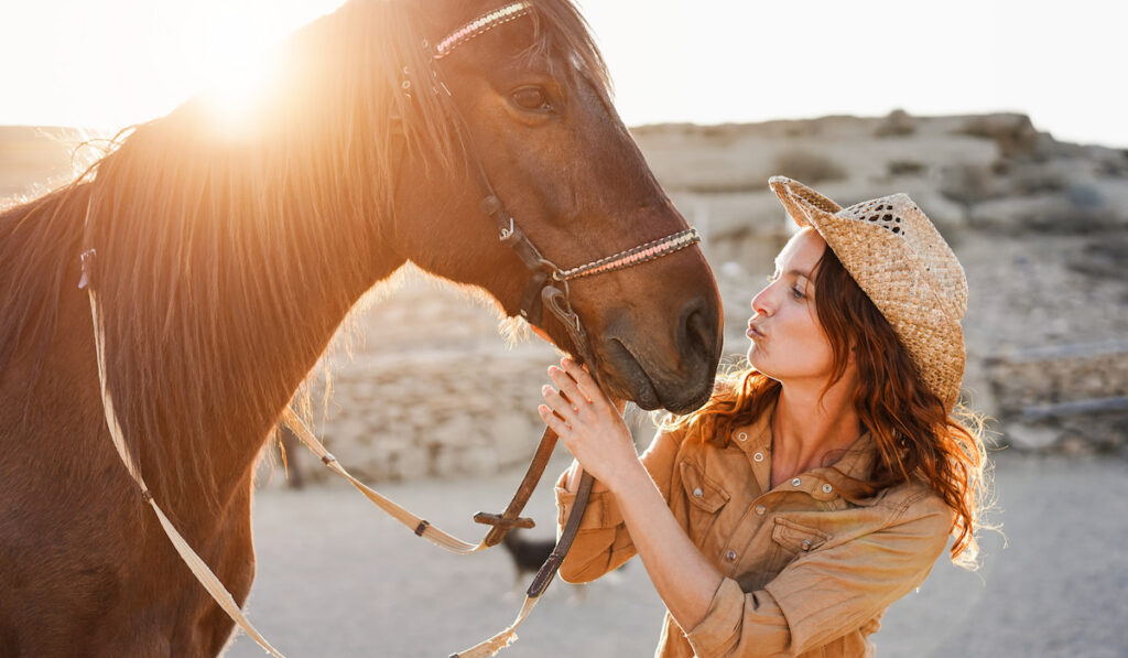 Young woman having tender moment kissing her horse at farm ranch